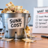 Leaking bucket filled with money illustrating the sunk cost fallacy in marketing budgets and underperforming advertising campaigns.